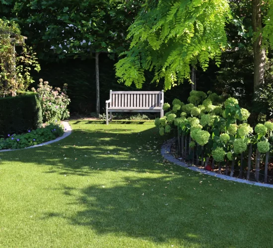 Coin agréable avec un banc de jardin sur du gazon synthétique Royal Grass dans un jardin très naturel avec beaucoup de plantes